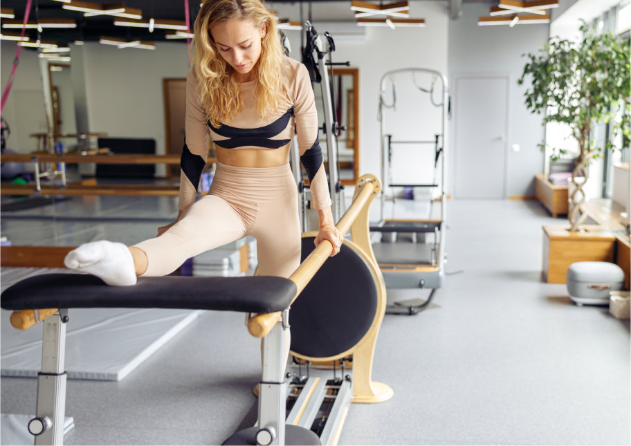 Healthy focused woman practicing pilates, having reformer training in stretching studio in the daytime. Flexibility, workout concept