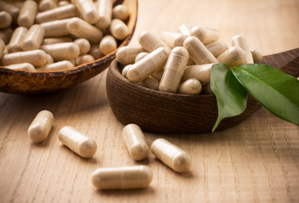 Alternative medicine tablets on a wooden spoon, green leaf.